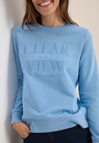 Sweatshirt bleu clair en tissu doux, avec du texte en relief "REFLET DE L'ESPRIT CLAR" sur le devant. Poignets et ourlet côtelés.