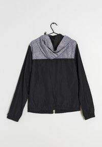 Black lightweight jacket with a gray fabric upper section and hood. Features elastic cuffs and a drawstring hem, hung on a black hanger.