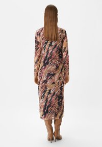 Langes, figurbetontes Kleid mit langen Ärmeln, das ein mehrfarbiges abstraktes Muster in warmen Tönen aufweist. Kombiniert mit beigefarbenen Stiefeln bis zum Knie.