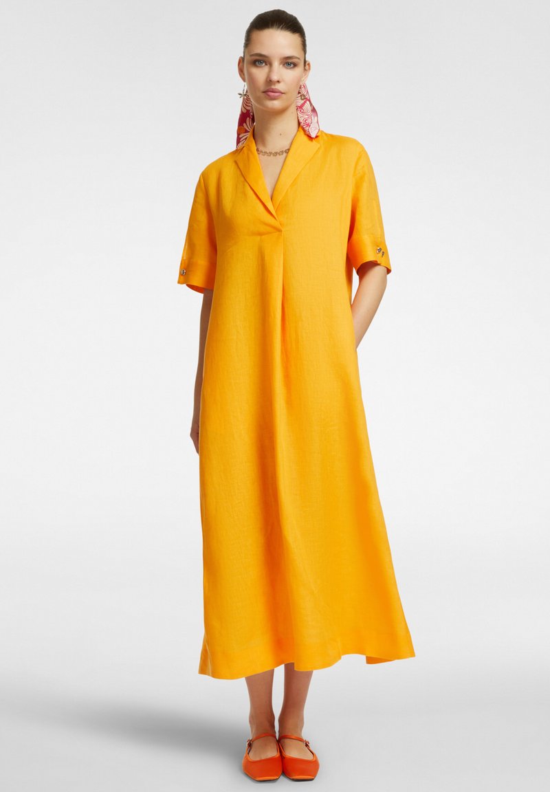 Abito in lino giallo con colletto, maniche corte e dettagli plissettati. Abbinato a scarpe arancioni e accessorio a motivi rosa nei capelli.