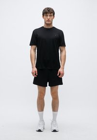 Set format din tricou și pantaloni scurți atletici negri, confecționat dintr-un material ușor care evacuează transpirația, având un design simplu, purtat cu adidași și șosete albe.