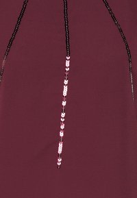 Bordeaux stof med en lodret linje af skiftende sorte og pink pailletter. Teksturen er glat, med en let glans fra pailletterne.