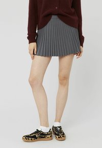 Jupe plissée grise avec une taille ajustée ; portée avec des baskets noires à imprimé léopard et des chaussettes blanches jusqu'à la cheville. Détail de tissu texturé visible.