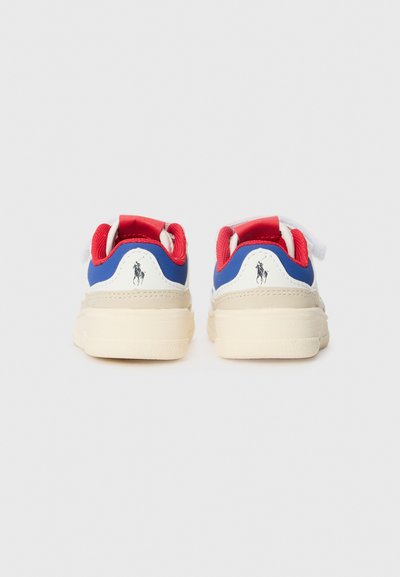 Zapatillas con parte superior blanca, acentos en azul y rojo, y suela beige. Presentan un lazo de tela roja, cordones blancos y un pequeño logotipo en el talón.
