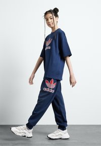 T-shirt oversized azul marinho e calças de fato combinando com o logo vermelho da Adidas e design trefoil. Sapatos atléticos brancos com detalhes cinzas.