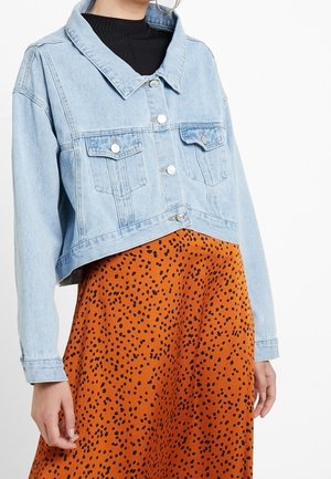 Ljusblå denim jacka med cropped längd, två bröstfickor, silverknappar och en klassisk krage, bärs över en orange prickig kjol.