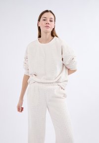 Suéter de color beige claro con un patrón de punto trenzado texturizado, combinado con pantalones sueltos a juego. Material suave y esponjoso; diseño relajado.