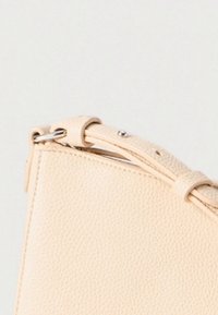 Beige skinnveske med teksturert finish, som har en strukturert form og kort stropp med metalliske detaljer.