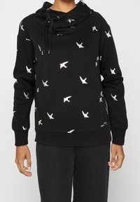 Sudadera negra con cuello de cowl, con patrones plateados de aves por toda la prenda. Está hecha de una tela suave con puños y dobladillo acanalados.