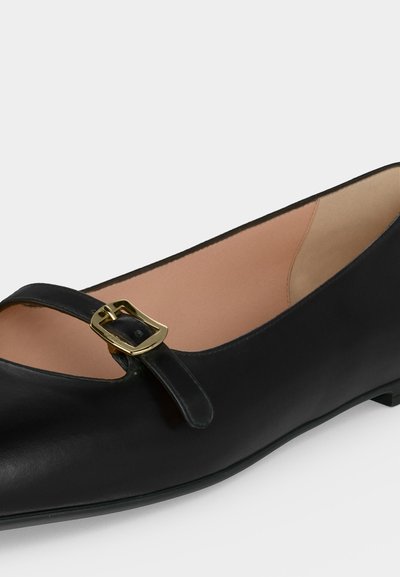 Μαύρο δερμάτινο Mary Jane flat παπούτσι με λεπτό λουράκι και χρυσή τετράγωνη αγκράφα, με στρογγυλεμένη μύτη και χαμηλό τακούνι.
