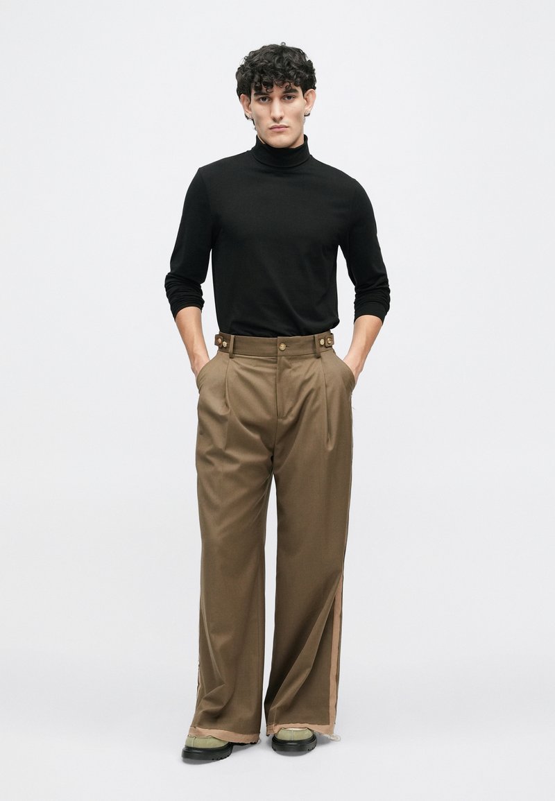 Sort turtleneck parret med højtaljede, lysebrune, brede bukser med sideslids og guldknapdetaljer.