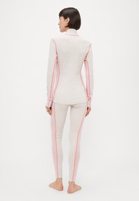 Εφαρμοστή μπλούζα με μακριά μανίκια και κολάν σε ανοιχτό ροζ χρώμα με διακριτικό μοτίβο, διακοσμημένα με έντονες ροζ ραφές και ψηλό γιακά για μια κομψή εμφάνιση.