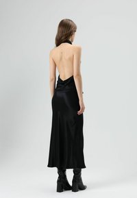 Zwarte satijnen halterjurk met een open rug en een vloeiende silhouet, gecombineerd met kniehoge zwarte laarzen met hak. Gladde textuur.