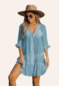 Robe chemise bleu clair à boutons, en tissu doux et texturé, avec des manches retroussées et un ourlet volanté.