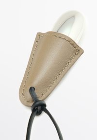 Custodia in pelle color taupe con cuciture a vista, contenente un oggetto arrotondato liscio di colore argento e bianco; fissato con un cordoncino nero.