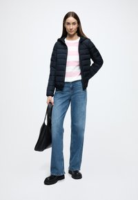 Ναυτικό μπουφάν puffer με κουκούλα πάνω από ροζ και λευκό ριγέ πουλόβερ, συνδυασμένο με ανοιχτό μπλε τζιν παντελόνι με φαρδιά μπατζάκια και μαύρα μποτάκια με χοντρή σόλα.