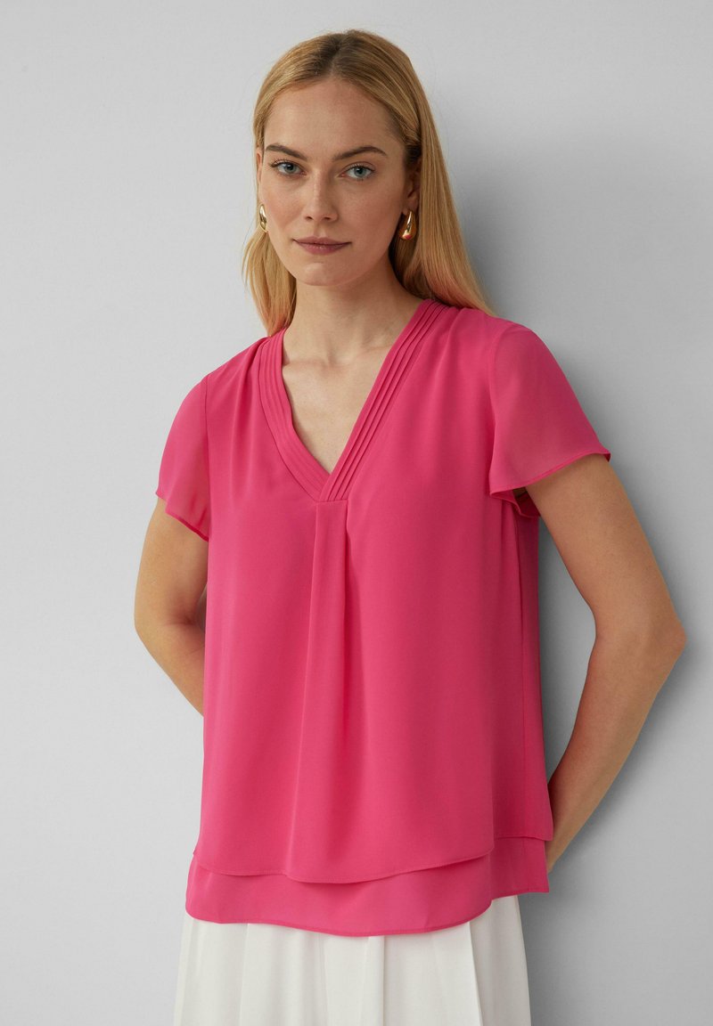 Fuchsia Kurzarmoberteil mit V-Ausschnitt, das Falten an der Brust und einen geschichteten Saum aufweist. Hergestellt aus leichtem, glattem Stoff.