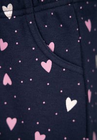 Navy fabric featuring small pink and white hearts and dots. Includes a side pocket with a smooth texture. Casual design, stretchable material.