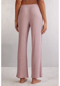 Ljusrosa ribbade loungebyxor med en avslappnad passform, med vid bendesign och elastisk midja, placerade mot en mjuk bakgrund.