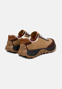 Sneaker marroni e beige con parte superiore testurizzata, suola nera e pattern di trazione in gomma. Presentano un design curvo e massiccio con accenti a contrasto.