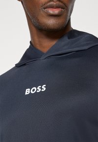 Mornarica dukserica s mekom teksturom, koja ima bijeli "BOSS" logo na prsima i minimalistički dizajn.