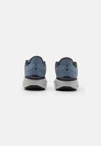 Des chaussures de sport bleues avec une tige en maille texturée, des accents noirs et une semelle en caoutchouc gris clair. Présente un passant au talon et un détail de logo contrastant.