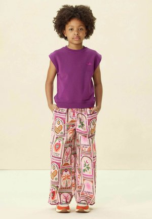 Paarse mouwloze sweatshirt met een subtiel logo, gecombineerd met brede, gestreepte roze broek met bloemen- en fruitontwerpen, aangevuld met multiculturele sneakers.