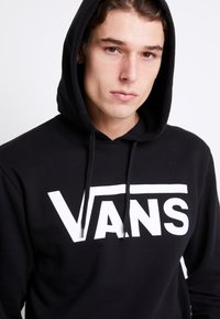 Felpa nera con cappuccio realizzata in tessuto morbido, caratterizzata da un grande logo bianco "VANS" sul davanti, con cappuccio regolabile e polsini a coste.
