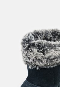 Kotníková obuv s tmavou semišovou úpravou a šedým umělým kožíškem na lemu, která se vyznačuje měkkou texturou a kulatým otvorem nahoře.