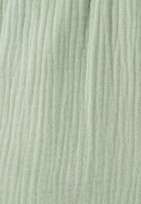 Tela de color verde claro con textura y un patrón de superficie arrugado, fabricada con un material suave y transpirable, que presenta ondulaciones verticales en toda su extensión.