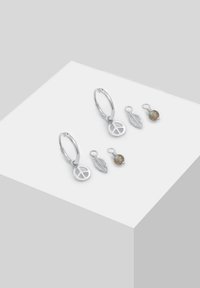 Orecchini a cerchio in argento con charm a forma di simbolo della pace, con due charm intercambiabili: una foglia in argento e una perlina in pietra. Texture liscia; finitura brillante.