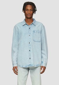 Lichtblauwe denim shirt met lange mouwen, knoopsluiting aan de voorkant en borstzak. Het heeft een relaxte pasvorm en een licht gescheurde zoom.