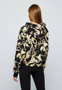 Sudadera con capucha negra y dorada con un patrón de mármol en espiral; cuenta con puños y dobladillo acanalados, texto del logo en la parte posterior.