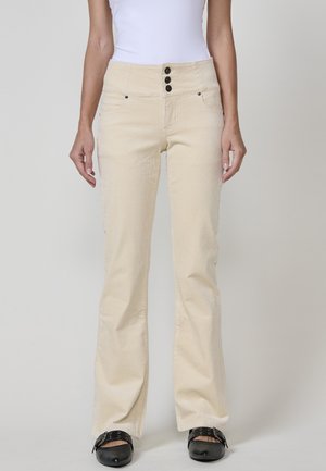 Los pantalones de pana de campana en color beige presentan una cintura alta con tres botones negros, dos bolsillos frontales y un diseño acanalado texturizado.