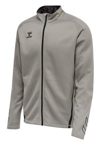 Jasnoszara sportowa kurtka zapinana na zamek z czarnym suwakiem, kieszeniami po bokach, czarnym logo hummel na lewej stronie klatki piersiowej oraz paskami na rękawach.