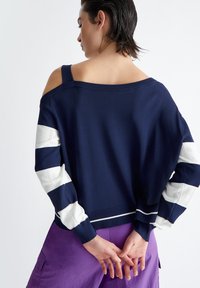Maglione blu navy con maniche a righe bianche, dettagli aperti sulle spalle, polsini a costine e vestibilità rilassata.
