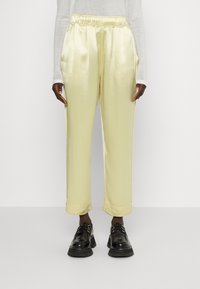 Satinbyxor i blekgul med elastisk midja och sidofickor, med en lös passform och uppvikta muddar, i kombination med svarta skor.