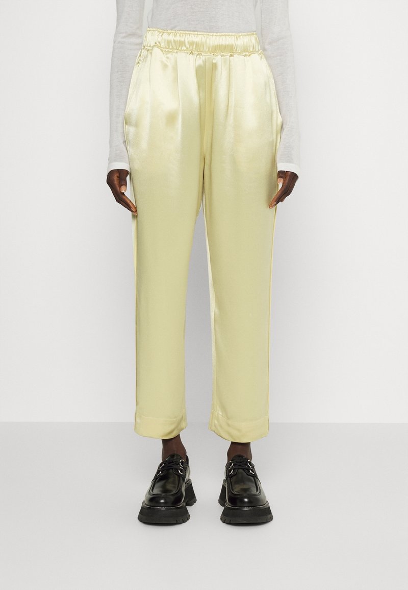 Satinbyxor i blekgul med elastisk midja och sidofickor, med en lös passform och uppvikta muddar, i kombination med svarta skor.