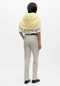 Svijetlo žuta pletena šala pada preko ramena, nosi se preko bijele košulje. Svijetlo sivi krojeni hlače i crne cipele upotpunjuju odjevnu kombinaciju.