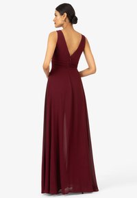 Langes burgunderfarbenes Kleid mit V-Ausschnitt, ärmellosem Design und gerafftem Taillenbereich. Hergestellt aus einem glatten Stoff mit einem fließenden Rock, der elegant fällt.