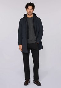 Námořnický kabát s kapucí přes šedý svetr, kombinovaný s černými kalhotami a tmavými botami. Jednotná textura, jednoduchý design, funkční knoflíky.