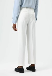 White tailored trousers with a straight leg design, detailed stitching, and visible back pockets, paired with black suede shoes.