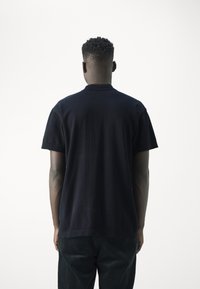 Camisa polo de algodón negra con mangas cortas, diseño liso y un cuello clásico. Presenta un corte relajado y se lleva con pantalones oscuros de textura.