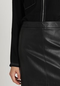 Svart läderpennkjol med en slät textur och rena linjer, kombinerad med en svart topp med en dragkedja och kontrasterande vit sömnad.