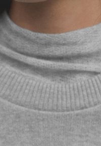 Pull à col haut gris avec un tissu texturé et doux ; doté d'un ourlet côtelé et d'une finition lisse, soulignant un design confortable.