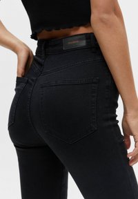 Jean taille haute noirs en denim, dotés d'une texture lisse, de coutures classiques et d'une étiquette de marque au dos de la taille.