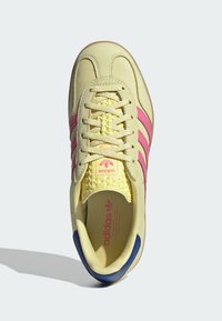 Tenisice s gornjim dijelom od žutog kože, ružičastim trakama, teksturiranim žutim jezikom i plavim naglaskom na peti. Zatvaranje na vezanje i brendirana unutrašnjost.