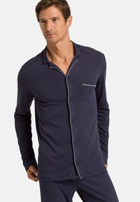 Navyblaues Langarm-Pyjamaoberteil aus glattem Stoff, mit Knopfleiste, eingeschnittenem Kragen und einer Brusttasche mit weißen Paspel-Details.