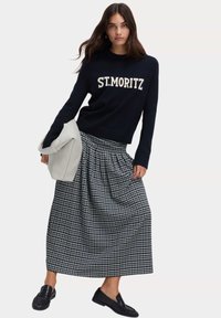 Granatowy sweter z napisem "ST. MORITZ", czarno-biała w kratę maxi spódnica z plisami, szara torebka oraz czarne mokasyny.