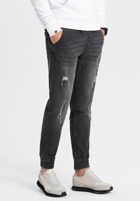 Joggers de mezclilla gris con puños elásticos, presentan detalles desgastados y un ajuste holgado, combinados con zapatillas gris claro.